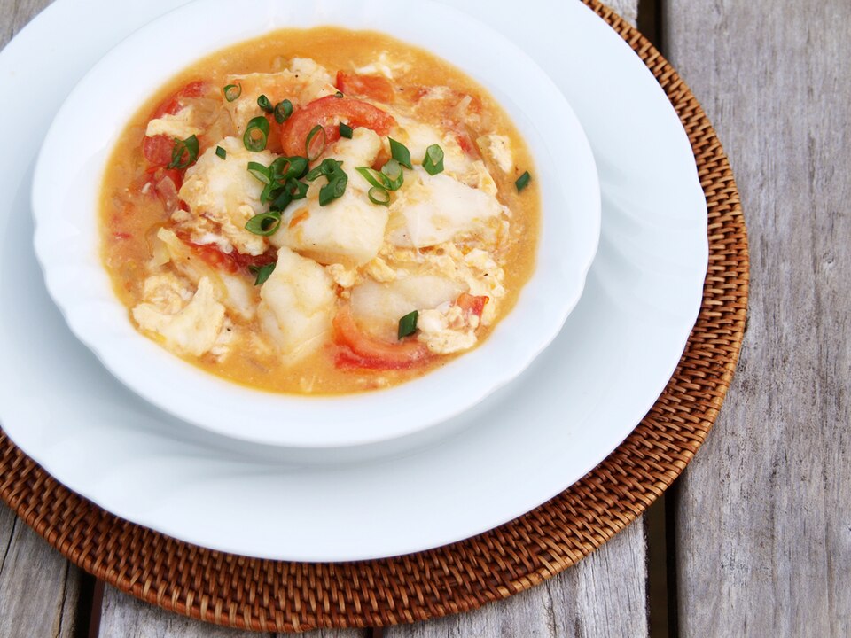 The dish is served in a bowl, with fish cooked in a tomato-based sauce that gives it a reddish hue.