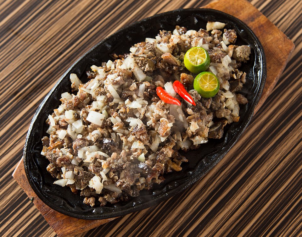 The dish is served on a cast iron sizzler with chopped meat on it. It's garnished with chili peppers and a calamansi.